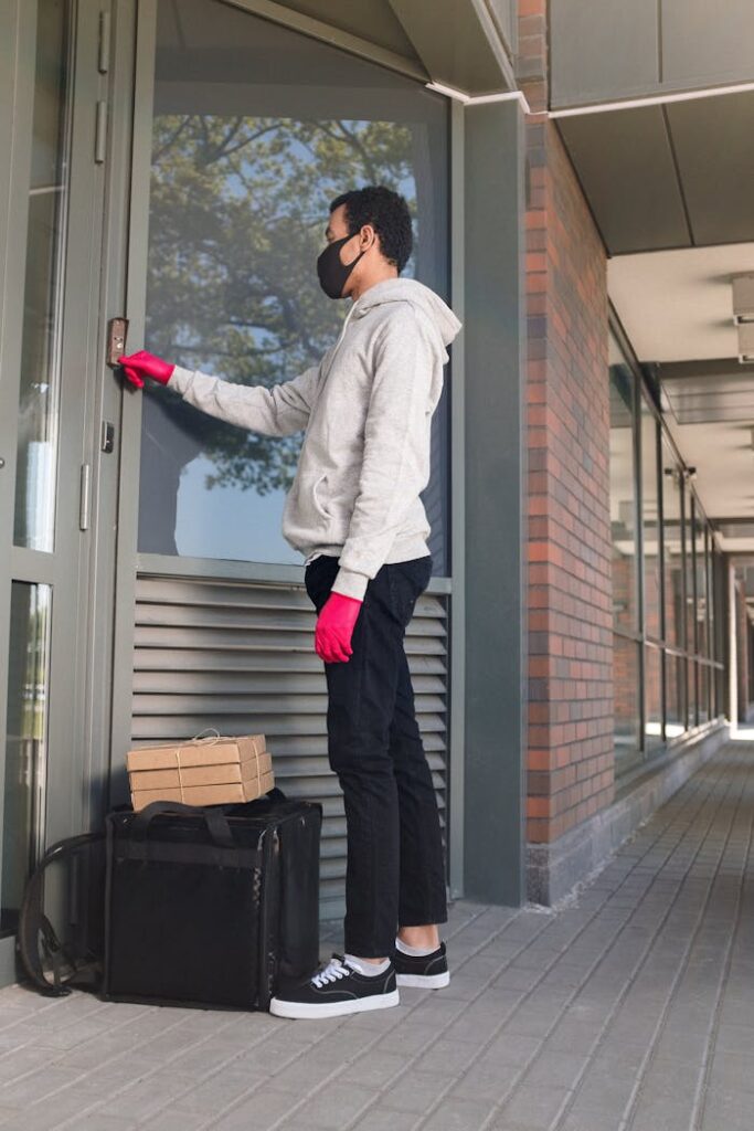 Courier in mask rings a doorbell for food delivery. Outdoor, casual urban setting, safe service.