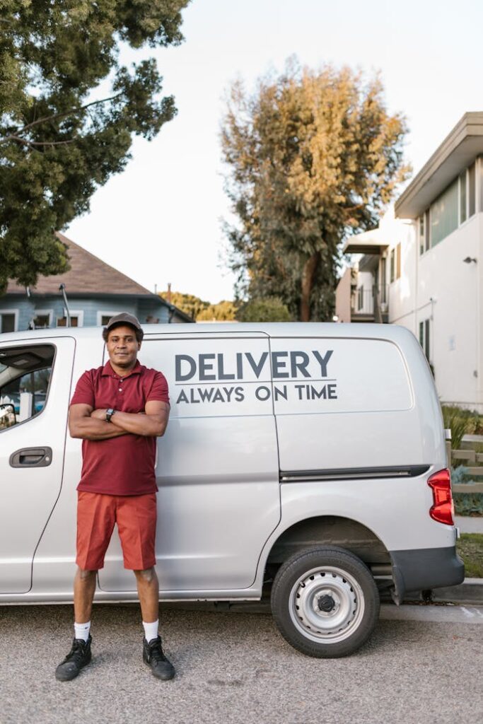 Confident delivery driver in uniform standing beside a punctual delivery service van outdoors.